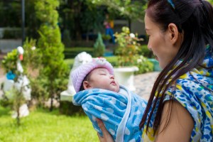Mum sings a lullaby to her baby who is wrapped in a blue shawl and with a pink hat on.