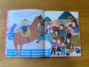 This shows one of the illustrated pages from the book. In this illustration Dolly Parton is riding a horse in a pen. She is watched by members of her large family. 