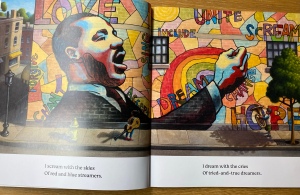 The illustration shows a bright, colourful mural full of rainbows  and colourful words like “Include” and “dream”. A black man in the mural is speaking, maybe preaching all about change. 