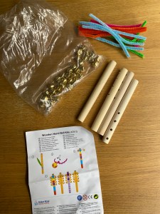 This shows the contents of the kit - individual small gold bells; pipe cleaners; wooden sticks with pre-drilled holes and a set of instructions